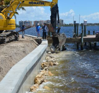 Excavator operator dropping pieces of riprap along seawall. Williamson and Sons recommends riprap for anyone on the river or on a waterway with heavy boat traffic.