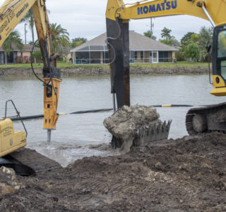 The excavator on the left side has been converted to an air hammer and is breaking the limestone ledge, while the second is clearing the broken pieces. Not only does this ensure a solid foundation for the new seawall but it will also give the watercraft full access to the property line.